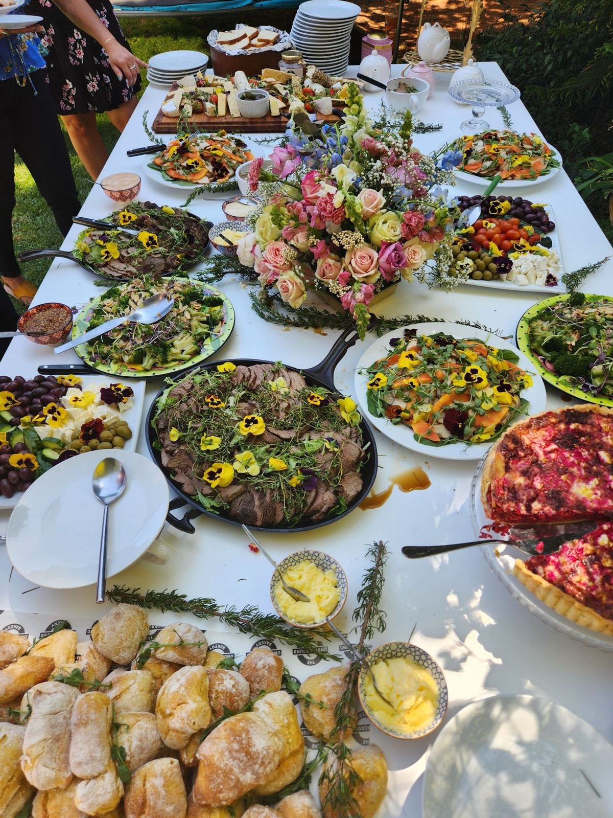 A long outdoor buffet table of salads, breads and flowers